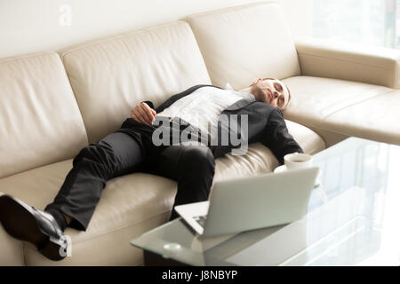 Tired businessman sleeping on sofa in office Stock Photo