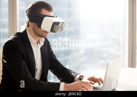 Office worker typing on laptop in virtual goggles Stock Photo