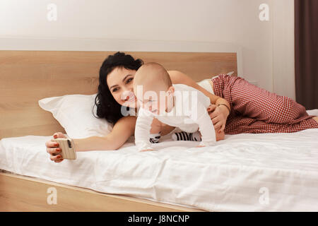 Happy smiling mother and baby lying on bed Stock Photo