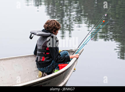 boy sitting in the front of a tin fishing boat with his fishing rods Stock Photo