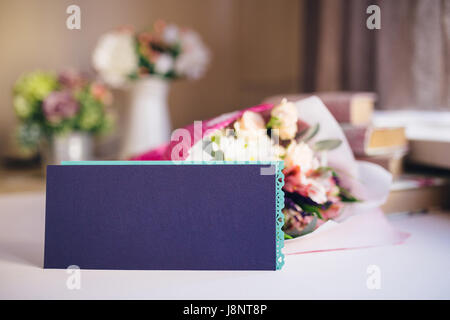 Flowers bouquets, blank violet envelope and stack of books on table Stock Photo