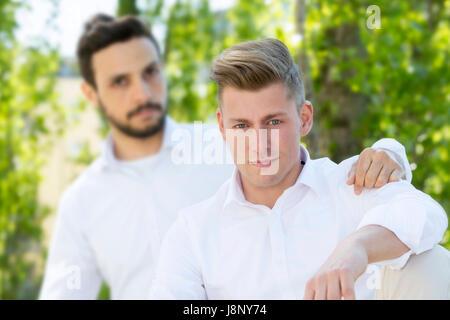 two handsome young man in white shirts sitting outside and smiling at camera Stock Photo