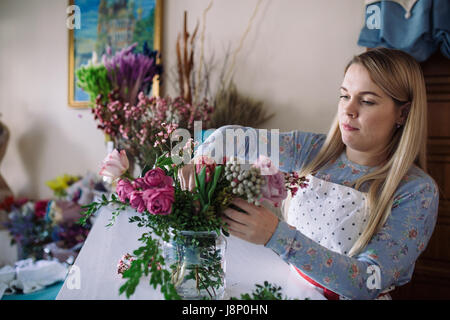 woman florist making bouquet of flowers indoor. Female florist preparing bouquet with roses, peony in flower shop