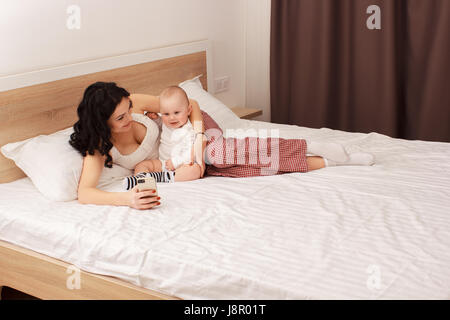 Happy smiling mother and baby lying on bed Stock Photo