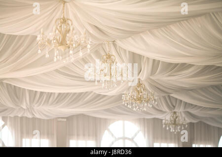 chandeliers on a ceiling, decorated by the draped white fabrics. a wedding decor in a white tent. Stock Photo