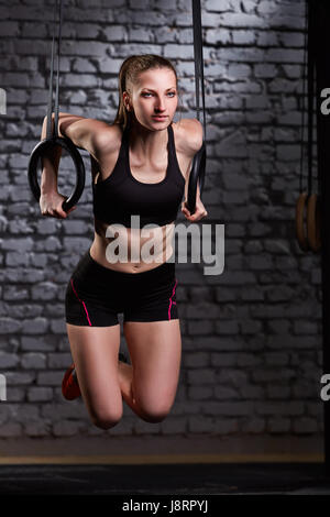 Image of beautiful young sporty woman in the black sportwear doing pull-ups exercise using gymnastic rings. Stock Photo