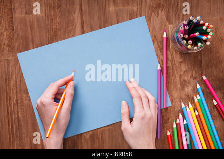 Human hands with pencil drawing something on the blue paper on wooden table Stock Photo