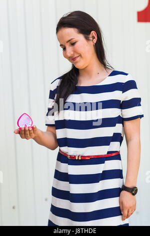 wedding, love, engagement and happiness concept - smiling woman in striped dress holding pink gift box with diamond ring over white background Stock Photo