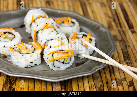 sushi pinwheels and wooden chopsticks on pewter plate and bamboo place mat Stock Photo