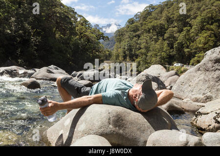 senior man resting on a rock by a river in Fiordland New Zealand Stock Photo