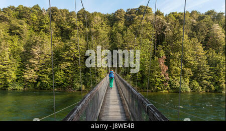 Female hiker crossing suspension bridge, Waiau river, Kepler Track, Fiordland National Park, Southland, South Island Stock Photo