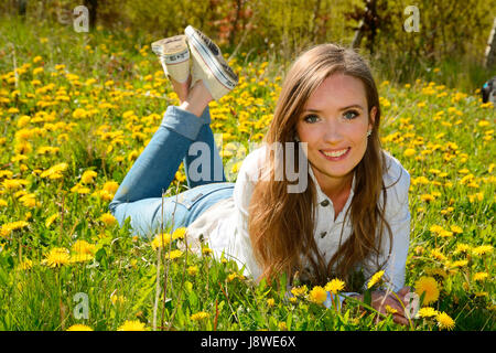 Young woman lying in a meadow of dandelion, Ystad, Scania, Sweden Stock Photo