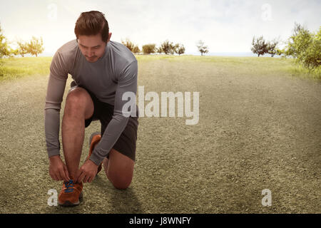 Handsome asian man kneeling tying running shoes getting ready for jogging on the park Stock Photo