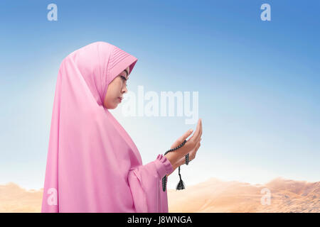 Religious asian muslim woman wearing veil praying with sunlight at sky Stock Photo