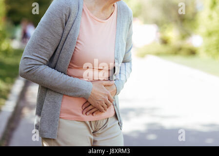 Upset old woman having sudden pain in the stomach outdoors Stock Photo
