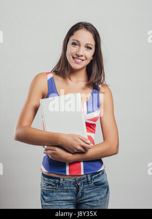 Smiling young girl wearing a British flag tank top and holding an hardcover book, language learning and education concept Stock Photo