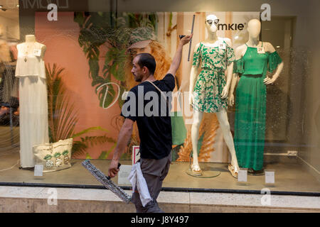 A window cleaner wipes soapy glass of a clothing retailer, on Pont de Marchands, on 23rd May, 2017, in Narbonne, Languedoc-Rousillon, south of France Stock Photo