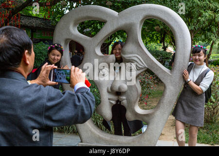 Guilin, China.  Elephant Trunk Hill Park.  Man Taking Picture of Three Women with Modern Sculpture Representing Love. Stock Photo