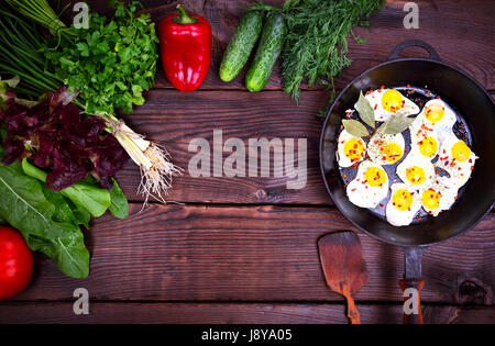 Fried quail eggs in a black cast-iron frying pan, opposite fresh vegetables and herbs Stock Photo