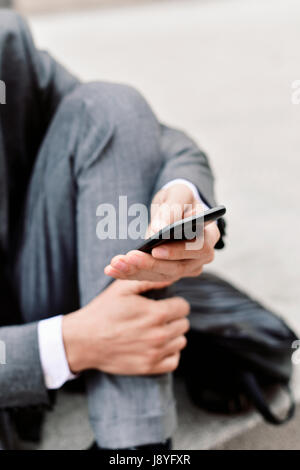 closeup of a young caucasian businessman in a gray suit using a smartphone outdoors Stock Photo