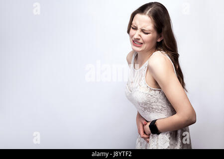 Portrait of beautiful woman with freckles and white dress and smart watch with stomach pain on silver gray background. healthcare and medicine concept Stock Photo