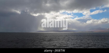 Reflected sunlight on Oban Bay with threatening skies above the Isle of Mull, Argyll and Bute, Scotland, United Kingdom. Stock Photo