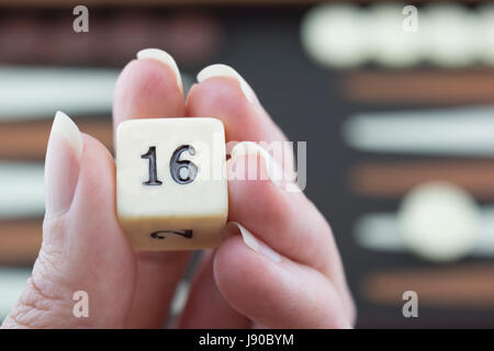 Readying to roll backgammon dice on the brown and cream backgammon board blurred in the background. Focusing on the dice in hand. Stock Photo