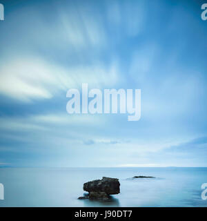 Dark rocks in a blue ocean under cloudy sky in a bad weather. Long exposure photography Stock Photo
