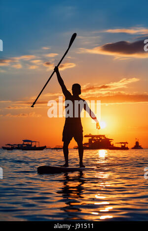 Paddle boarder. Black sunset silhouette of young sportsman paddling on stand up paddleboard. Healthy lifestyle. Water sport, SUP surfing tour in adven Stock Photo