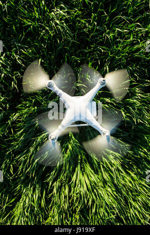 quadcopter summer flight outdoors, aerial imagery and recreation concept - superb modern white high-tech drone flying at low altitude on background of green field of grass, top view, vertical. Stock Photo