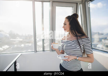 Smiling young businesswoman holding a coffee cup and looking out the window. Stock Photo
