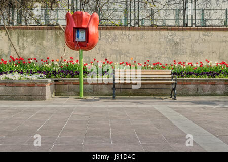 Tulip shaped public phone and wooden bench in front of built-in tulip flower box and grunge wall on tiled stone floor, Fatih district, Istanbul, Turke Stock Photo