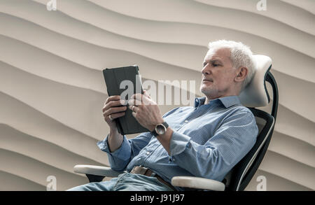 senior man sitting in luxury office chair using tablet Stock Photo