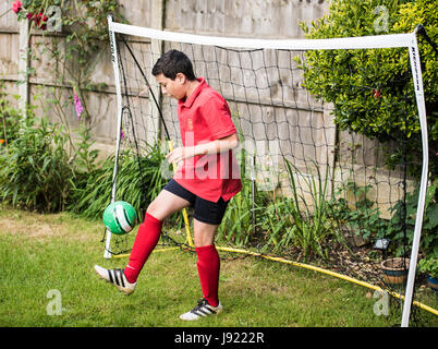 Boy plays football in garden, with goal net Stock Photo