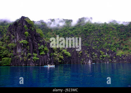 Filipino fishermen boating along steep cliff Karst rock formations near Alcatraz Reef in the island of Coron in the Calamian Islands in northern Palawan of the Philippines Stock Photo