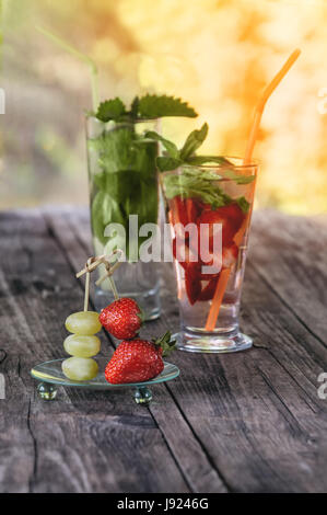 Strawberries and grapes on a skewer on the glass background with strawberry and grape detox drink on a wooden table on a Sunny day. The vertical frame. Selective focus. Stock Photo