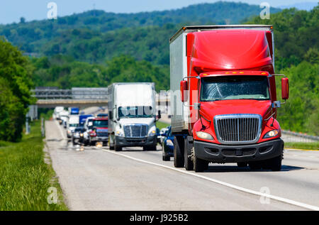 A red semi leads a line of traffic down an interstate highway in Tennessee.  Heat rising from the pavement gives background trucks and forest a cool s Stock Photo