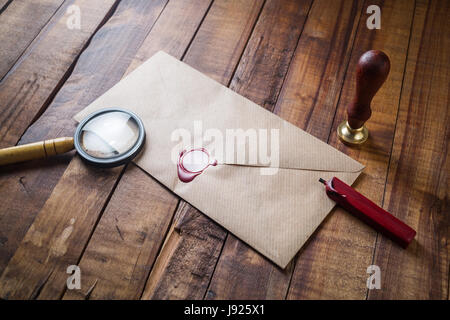 Craft paper envelope, magnifier, seal, stamp on vintage wooden table background. Template for placing your design. Blank stationery. Stock Photo