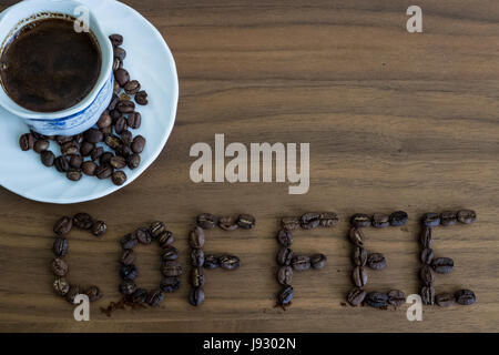 Roasted coffee beans, scattered on the table and written Coffee, in a cup of roasted, over coffee, brown wood texture, background wood, plates of tabl Stock Photo