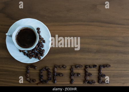Roasted coffee beans, scattered on the table and written Coffee, in a cup of roasted, over coffee, brown wood texture, background wood, plates of tabl Stock Photo