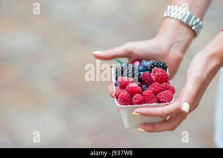 Close up berries fruits at female hands. Blueberries, raspberries, strawberries and blackberries on the market. Stock Photo