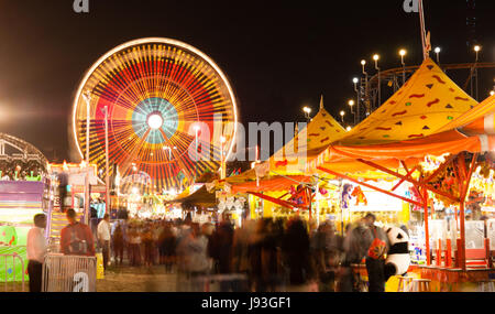 The midway is all lit up at night with motion occuring in this long exposure at the state fair Stock Photo