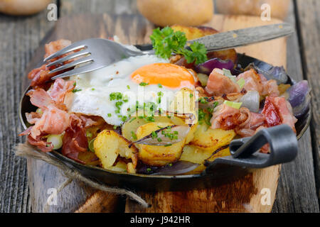 Farmer's breakfast with fried potatoes, fried egg and bacon served in an iron pan Stock Photo