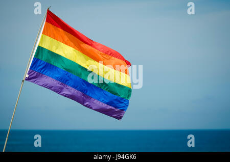 Gay pride rainbow flag flying outdoors in bright summer sun above the ocean horizon in Fire Island, New York Stock Photo
