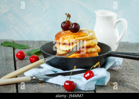 Homemade cottage cheese pancakes with cherries in a cast-iron frying pan. Russian dessert from cottage cheese. Stock Photo