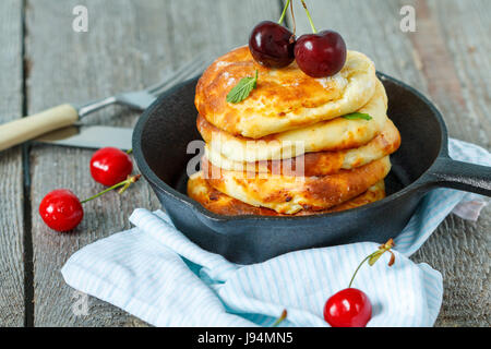 Homemade cottage cheese pancakes with cherries in a cast-iron frying pan. Russian dessert from cottage cheese. Stock Photo