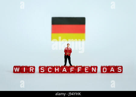 ILLUSTRATION - A small figurine of German Chancellor Angela Merkel stands under a German flag and on top of letter-dice spelling out 'WIR SCHAFFEN DAS' (WE CAN DO IT). Taken 18.03.2017. This quote dates back to a press conference with Angela Merkel on 31 August, 2015 that she made with regard to the refugee crisis in Europe beginning in 2015, and to Germany's accommodation of refugees. Since then, it has found far-reaching resonance within political debates and the media. It is the central slogan of the so-called 'Willkommenskultur' (Welcome culture). Merkel repeated the often-criticised phras Stock Photo