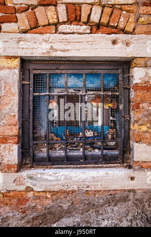 Italy,Venice,Isola di San Pietro. Window of Venetian house, crumbling,decerit,decaying brick wall, iron burglar bars & collection of quirky objects Stock Photo