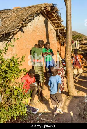 Malawian children stand by traditional grass roofed house in rural village of Kanyama, Malawi, Africa - NB Solar panel for recharging mobile phones