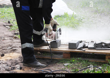 A working mason cuts the sidewalk tile with a circular saw while repairing the sidewalk in the city. Stock Photo